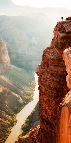 a man standing on the edge of a cliff overlooking a river and canyon below him