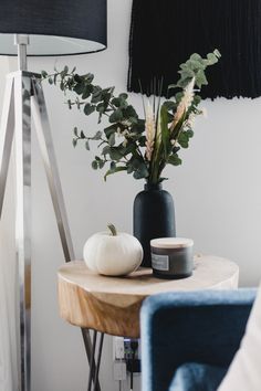 a table with a vase and some plants on it next to a blue chair in front of a white wall