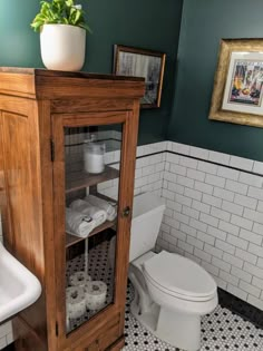 a bathroom with green walls and black and white tile flooring, a wooden cabinet over the toilet