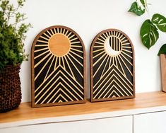 two wooden art pieces sitting on top of a white shelf next to a potted plant