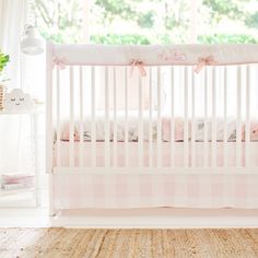 a baby crib with pink and white bedding in a room next to a window