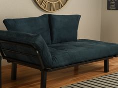 a blue couch sitting on top of a hard wood floor next to a wall clock