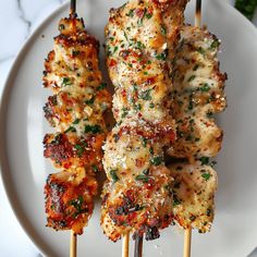 several chicken skewers on a white plate with parmesan cheese and herbs