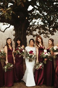 a group of women standing next to each other in front of a tree holding bouquets