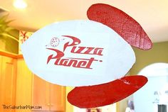 a pizza planet sign hanging from the ceiling in a kitchen with wooden cabinets and wood floors