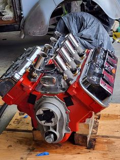 a red engine sitting on top of a wooden pallet next to a silver car