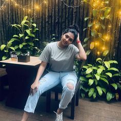 a woman sitting on top of a wooden chair next to a plant filled with potted plants