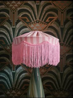 a pink table lamp with fringes on it in front of a wallpapered background