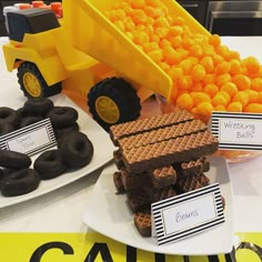 a table topped with chocolate covered donuts next to a dump truck filled with oranges