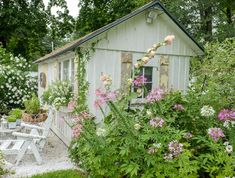 a garden shed with flowers growing around it and a picnic table in the foreground