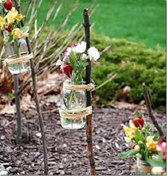 three mason jars filled with flowers on top of a rock garden path in front of a green lawn