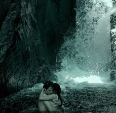 a woman sitting in the water next to a waterfall with her arms around her head