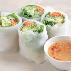 four rolls on a plate with dipping sauce in a small white bowl next to them