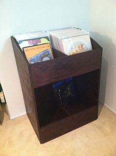 a wooden box with books inside on the floor next to a white wall and carpet