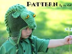 a young boy wearing a crocheted green hat and holding a dandelion