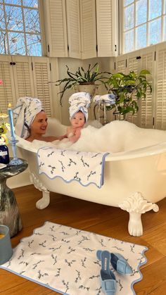 two baby dolls in a bathtub with towels and slippers on the floor next to each other