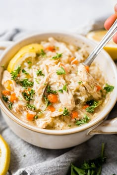 a bowl of chicken and rice soup with lemon wedges