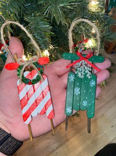 two popsicle ornaments are being held by someone's hand in front of a christmas tree