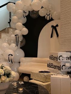 white balloons are hanging from the ceiling in front of a table with flowers and gifts