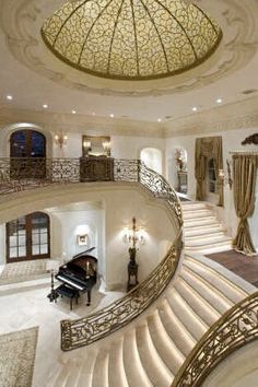 an image of a grand piano in the middle of a room with stairs and chandelier