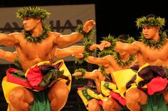 two men in hula skirts are dancing on stage with wreaths around their necks