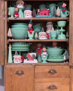 a wooden cabinet filled with lots of green dishes and santa clause figurines on top of it