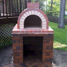 an outdoor brick pizza oven in the middle of a yard with grass and trees behind it