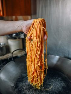 someone is holding up some noodles in a frying pan