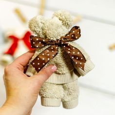 a hand holding a small teddy bear with brown polka dots on it's bow