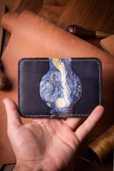 a hand holding a wallet with a painting on it