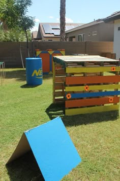 some wooden crates sitting in the grass near a blue trash can and a palm tree