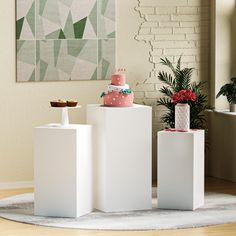 three white pedestals with cakes on them in front of a painting and potted plant