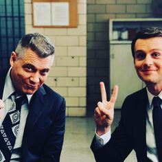 two men in suits and ties making the v sign with their fingers while sitting down