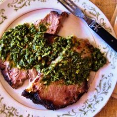 a white plate topped with meat covered in pesto next to a knife and fork