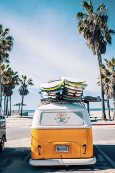 an orange and white vw bus with surfboards on the roof parked in front of palm trees