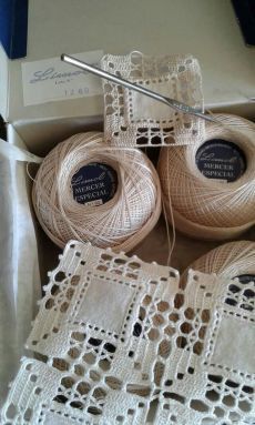 three balls of yarn are sitting in a box next to some crocheted doily