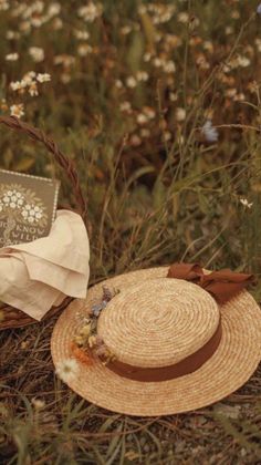 a straw hat sitting on top of a grass covered field next to a basket filled with flowers