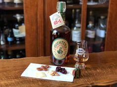 a bottle of liquor sitting on top of a wooden table next to a glass filled with nuts