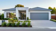 a white house with two garages and plants in the front yard on a sunny day