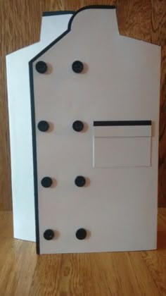 a paper house with black buttons on the front and white door that has holes in it