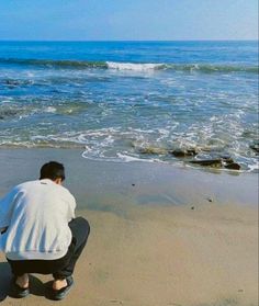 a man kneeling down on the beach next to the ocean