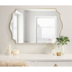 a mirror sitting on top of a white dresser next to a vase with a plant