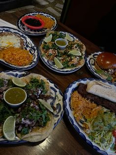 several plates with tacos, salads and condiments are arranged on a table