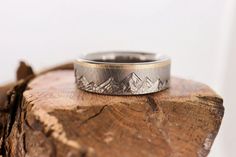 a wedding ring sitting on top of a piece of wood with mountains in the background