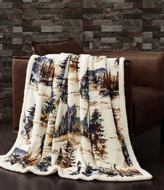 a couch with a blanket on it in front of a brick wall and brown leather chair