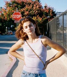 a woman standing on the side of a road with her hands on her hips and looking at the camera