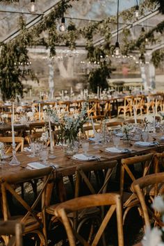 an outdoor wedding reception set up with wooden chairs and long tables covered in greenery