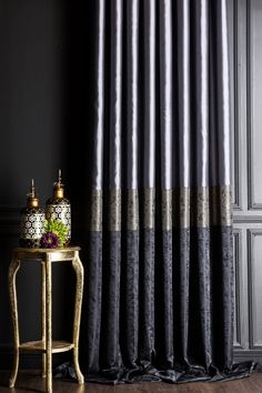 a table with a vase on top of it next to a black and gold curtain