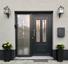 two planters with yellow flowers are in front of a black double door on a gray house