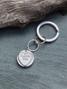 a heart shaped keychain with the words love you on it sitting next to a piece of driftwood